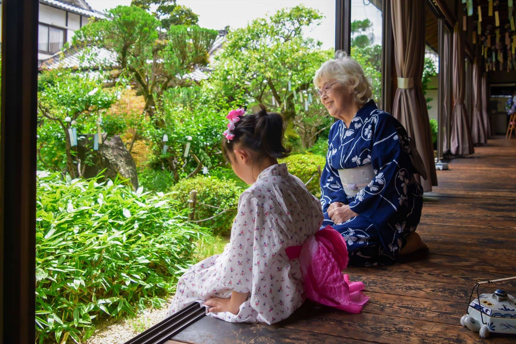Granddaughter and grandmother sitting on the porch of their house wearing yukata.