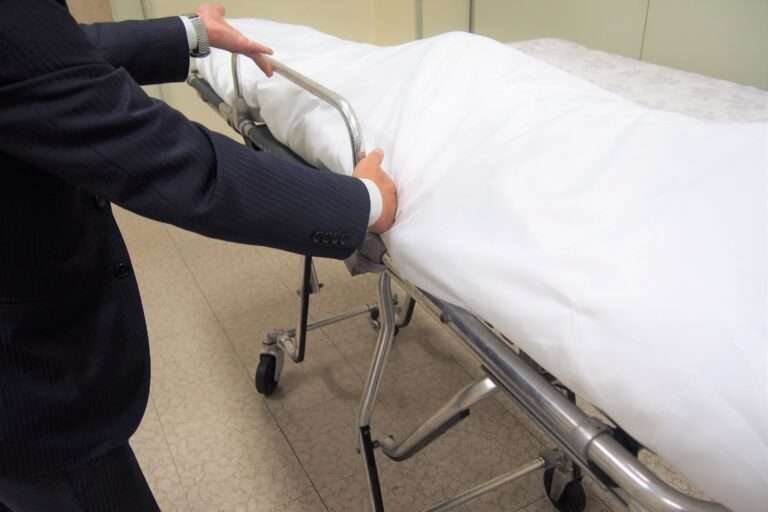 ストレッチャーに遺体を乗せ固定している葬祭ディレクター。