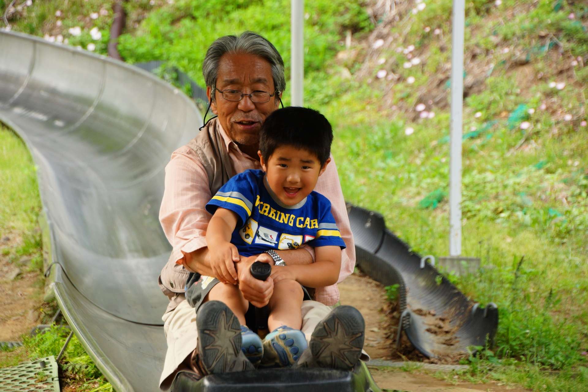 滑り台を一緒に滑って遊んでいる祖父と孫。